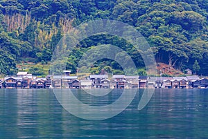 Traditional wooden boathouses line shore between calm bay and forested hills