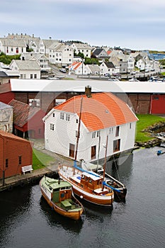 Traditional wooden buildings and three boats along the waterfront and the marina. Haugesund, Norway