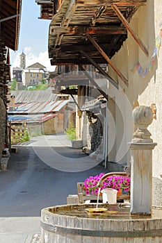 A traditional wooden fountain with traditional wooden balconies and the church in the background in Saint Veran village photo