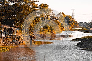 A traditional wooden t fishing trap with a golden orange beautiful forest along river in Thailand background