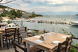 Traditional wooden tables and chairs of a greek tavern over the view of the port of Amaliapoli, Greece