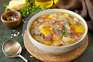Traditional Zelnacka cabbage soup with sausages and vegetables in a bowl on a stone tabletop. Czech cuisine
