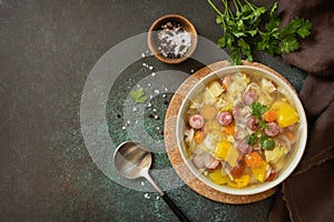 Traditional Zelnacka cabbage soup with sausages and vegetables in a bowl on a stone tabletop. Czech cuisine. View from above. Copy