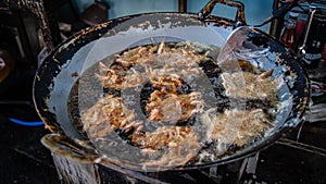 Traditionally battered shrimp are being fried in hot oil on a pan to be sold as food photo