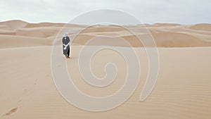 A traditionally dressed Moroccan Bedouin man walks in the sand dunes of Lac Naila, Morocco.