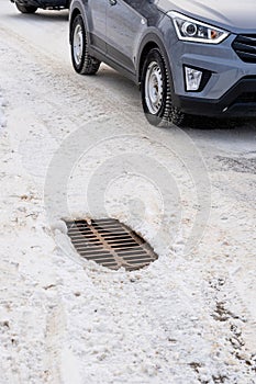 Traffic on asphalt covered with snow and sand. Storm sewer grate