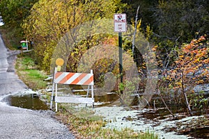 Traffic barricade with solar lamp and No Parking Any Time sign along a flooding lake during autumn