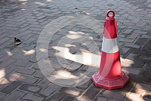 Traffic cone, with white and orange stripes on walkway.