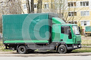 Traffic, delivery, a small green logistics truck on the road against the background of buildings.