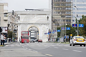 Traffic and doubledecker bus in front of Macedonian gate in Skopje which is one of the many monuments