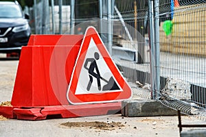 Traffic fence and a triangular sign with information about construction work on the roadway. Close-up