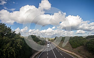 Traffic on the highway with cars and lights moving, seen from above, with a beautiful panorama of fields and mountains and clouds