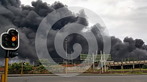 Traffic light in city with black toxic smoke in the background.