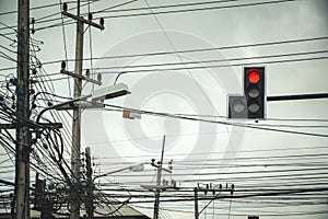 Traffic light at intersection roads showing red light with tangle of Electrical cables and Communication wires on electric pole