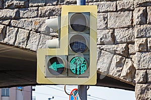 Traffic light with on left arrow section and a permissive green signal closeup on the background of arches of a stone bridge in photo