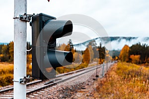 A traffic light at a level crossing with a yellow signal - autumn trees in brightly colored warm colors and gentle fog