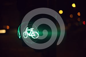 traffic light showing green bicycle symbol at night with colorful lights in blurred background