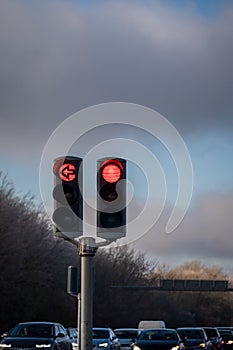 Traffic light showing red lights and left arrow with traffic behind against cloudy sky
