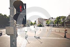 A traffic light shows a red pedestrian graphic in front of a wide city square with electric scooters and city buildings