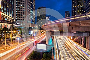 Traffic light and sky train in busy light trails at night.