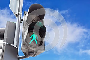 Traffic lights with the green light lit for pedestrians against blue sky background with clouds.