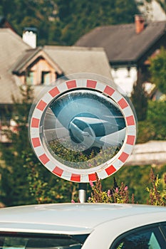Traffic mirror with a reflection of white car in scenic alpine village in summer