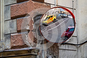 A traffic mirror with a yellow ambulance emergency car parked on the side of the street