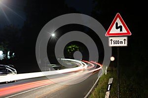 Traffic at night. A sign warns of curves.