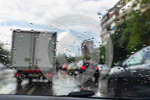 Traffic in rainy day with road view through car window with rain drops, blurry traffic on rainy day