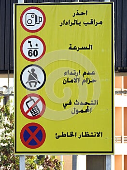 A traffic road sign in Arabic (traffic radar, maximum speed 60, seat belt, no cellphones, no parking) )