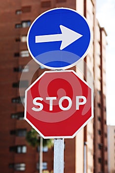 Traffic rules. Red road sign stop and blue and white right directional arrow on residential buildings background. Street