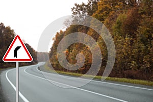 Traffic sign BEND TO RIGHT near empty asphalt road in autumn