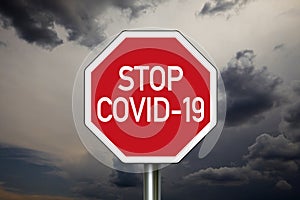 Traffic sign with dark cloudy sky with message Stop Covid 19