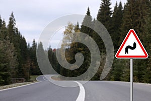 Traffic sign DOUBLE BEND FIRST TO RIGHT near empty asphalt road going through coniferous forest