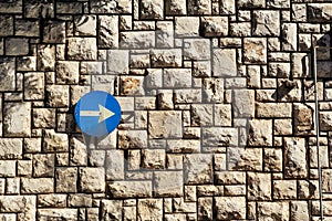 Traffic sign one way street sign with an arrow on a stone wall is a pattern of texture and material with colored stones.