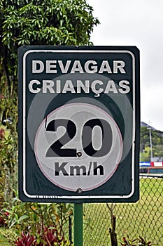 Traffic sign speed limit at 20 kilometers per hour with portuguese words that mean SLOWLY CHILDREN