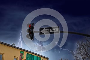 A traffic signal with a red light and a black and white one way sign with powerful storm clouds and lightning