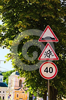 Traffic signs against green leaves linden tree at sunny morning. Warning Sign Children, Speed Limit Sign. Hump road sign post.