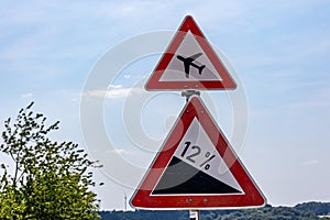 Traffic signs indicating: airport warning sign or low flying airplane and steep 12 percent downhill gradient in road