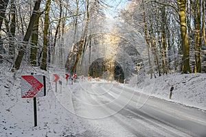 Traffic signs with red arrows on a dangerous curve on an snowy country road through the winter forest, safety driving concept,