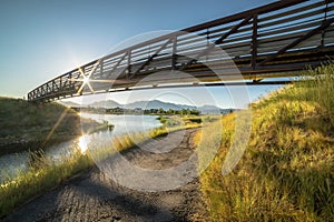 Trail along a lake and passing under a bridge with sun and blue sky overhead