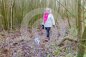 Trail between bare bushes with woman walking with her dachshund on muddy ground
