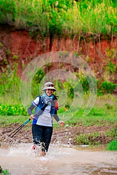 Trail runner, Asian woman wearing sportswear and equipment Practicing running and wading through water, running on a dirt path On
