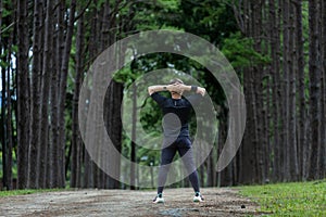 Trail runner in black clothe is stretching for warm up outdoor in the pine forest dirt road for exercise and workout activities