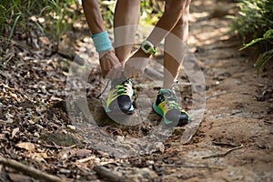 Trail runner tying shoelace in morning forest