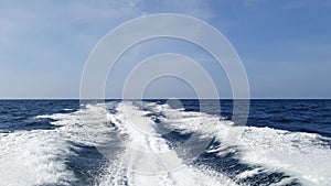 Sea wake trail behind a speed boat with waves, foam, bubbles on the ocean water surface with clear bright blue sky