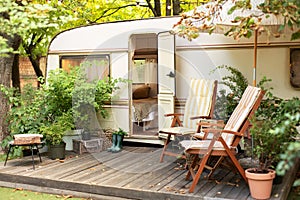 Trailer of mobile home stands in garden in camping. Backyard with RV house with garden furniture.