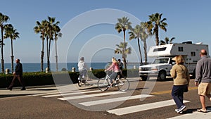 Trailer, people riding bikes, ped crossing zebra, waterfront road. Ocean beach palms, California USA