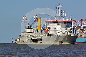 Trailing suction hopper dredger in the Weser estuary with container vessel and port facilities in the background