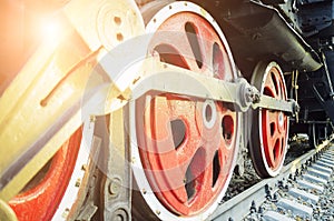 Train drive mechanism and red wheels of an old soviet steam locomotive. Bright rays of the setting sun